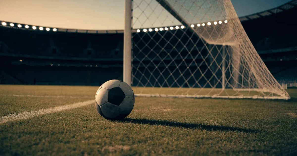 Ein Fußball liegt im Strafraum direkt vor dem Tor mit Netz, im Hintergrund leere Ränge bei Dämmerung.