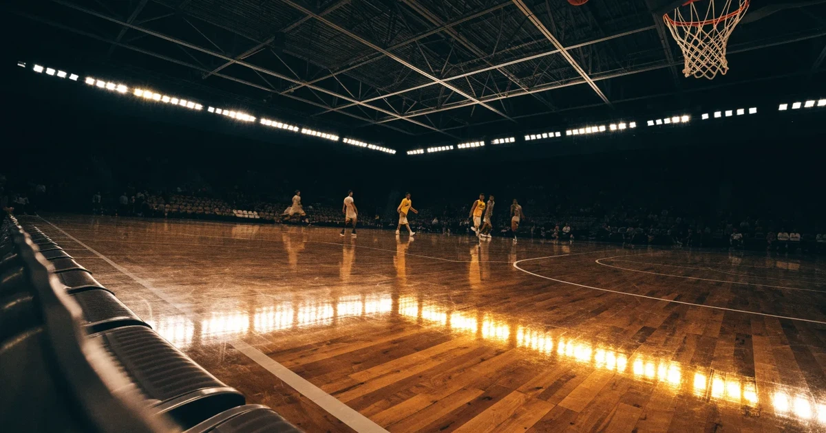 Eine leere Basketballhalle von einer oberen Tribünenreihe aus gesehen, Parkett und Körbe im Licht der Hallenstrahler.